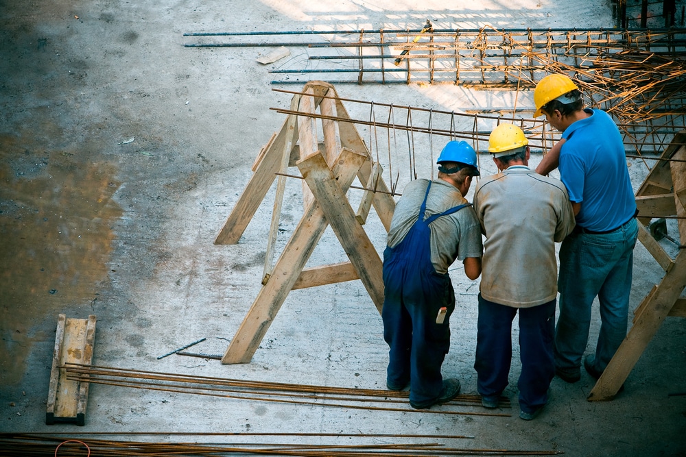 Construction workers reviewing plans on site near rebar framework